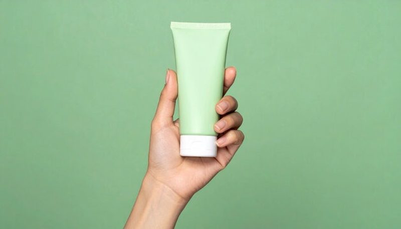 Original phone photo — a hand holding a cosmetic tube on a green background
